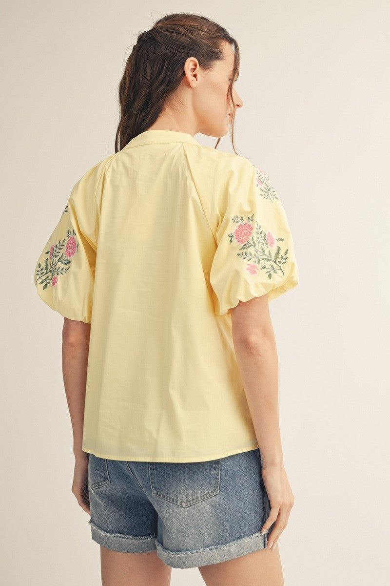 Back view of a woman wearing a yellow Hailey short puff sleeve V-neck top with floral embroidery.