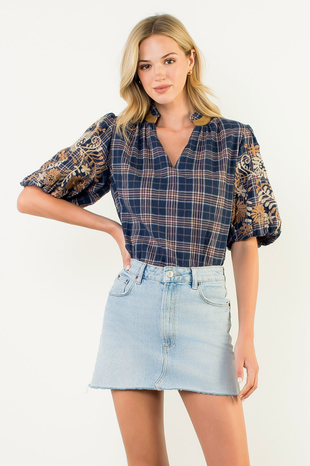 Woman wearing a Gwen blue gingham top with embroidered puff sleeves and a light denim mini skirt.