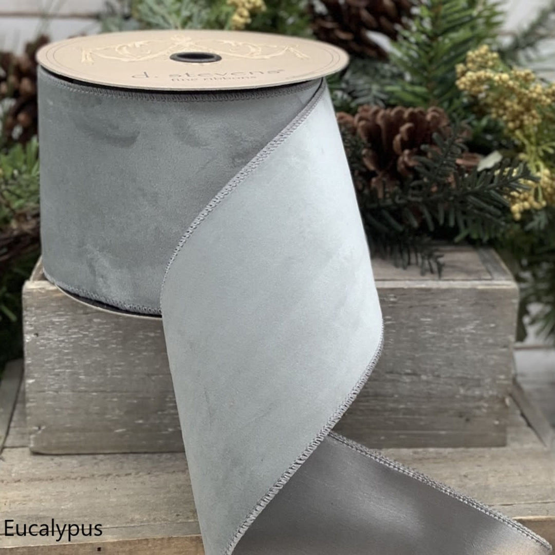A roll of 2.5-inch wide eucalyptus green velvet taffeta ribbon with a stitched edge.