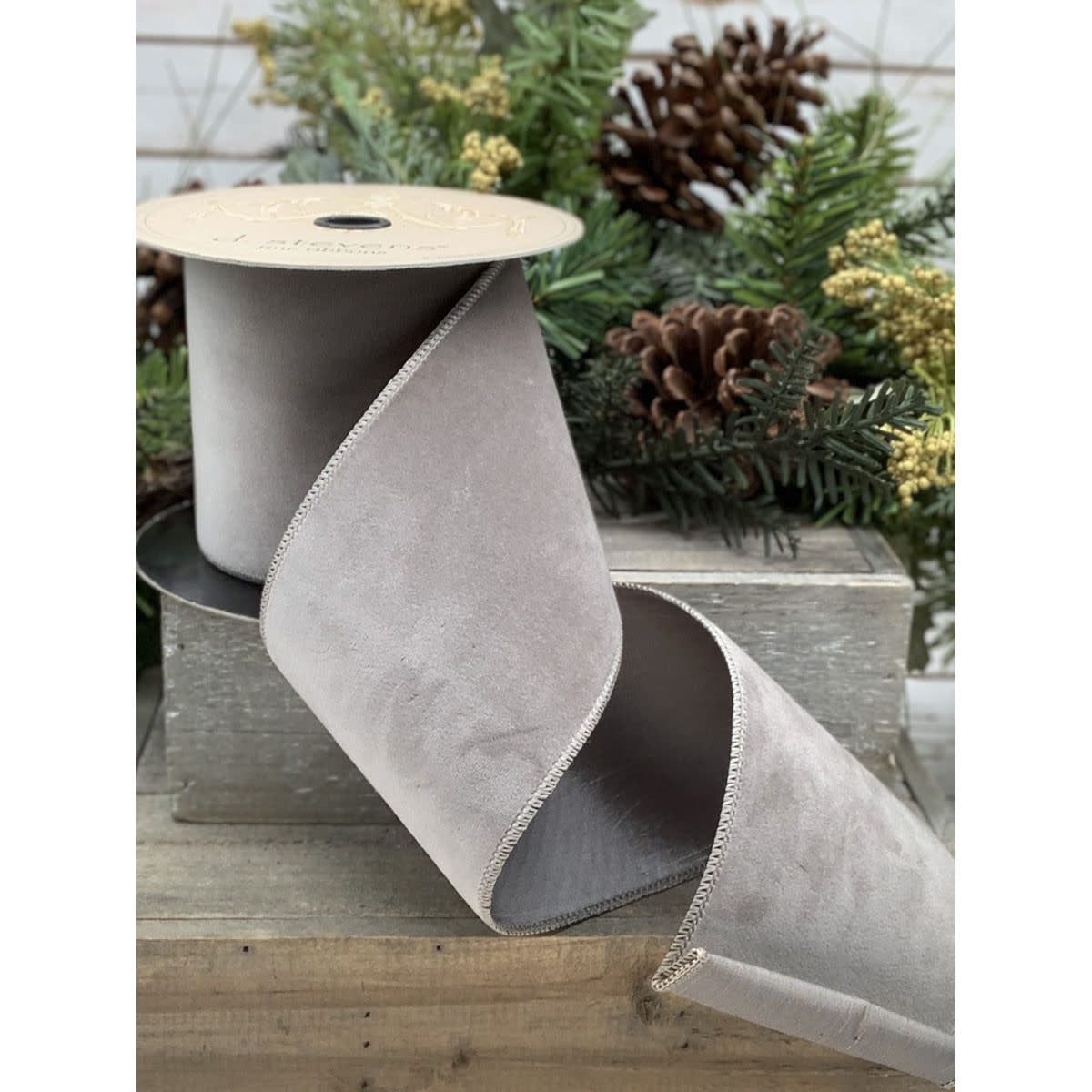 A spool of wide, light gray velvet ribbon with a taffeta backing and stitched edges.