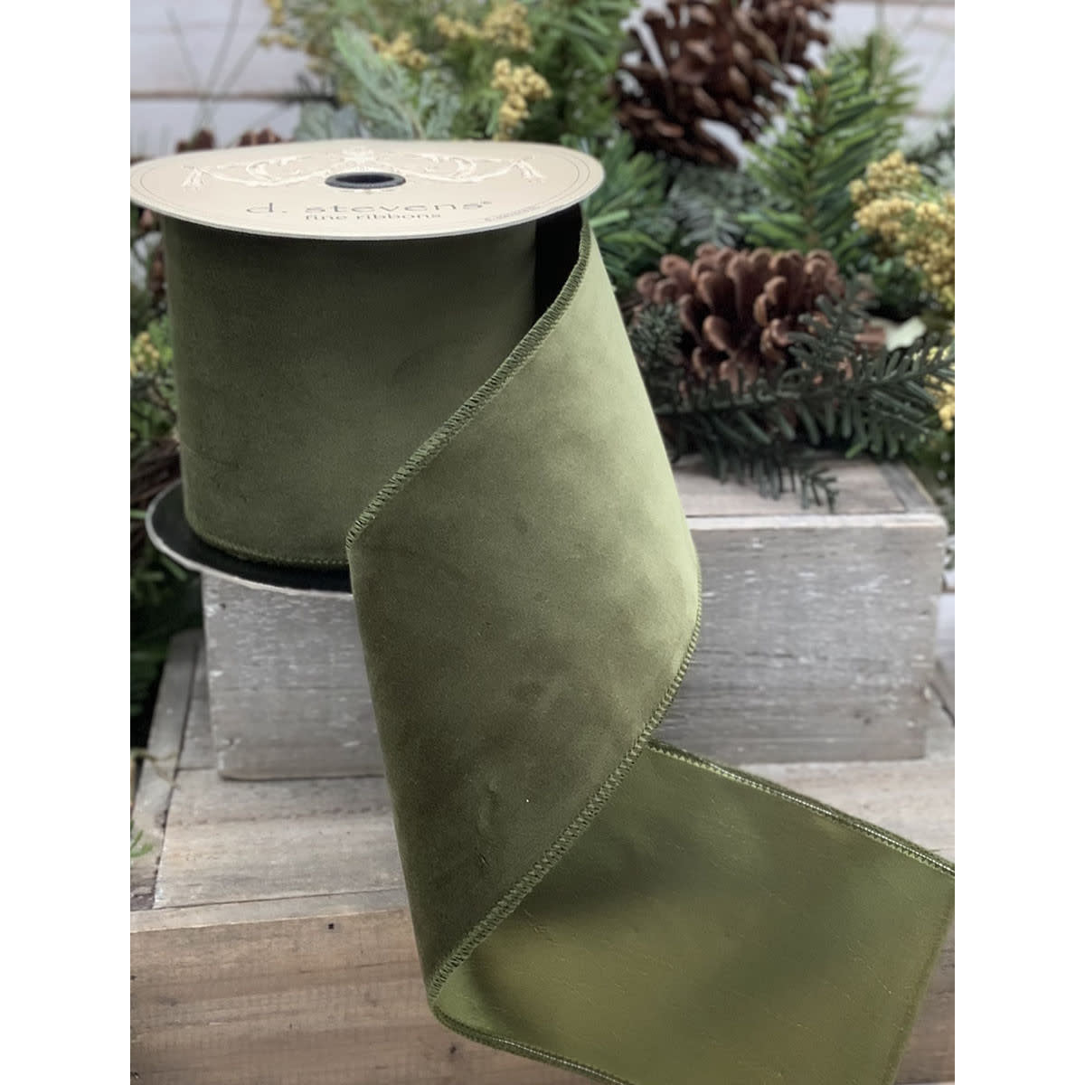 A roll of olive green velvet ribbon with a taffeta backing, displayed on a rustic wooden crate.