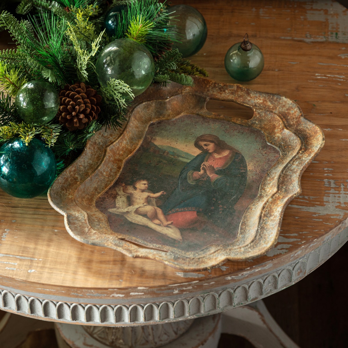 Vintage-style Madonna and Child metal tray with scalloped edges on a rustic wooden table.