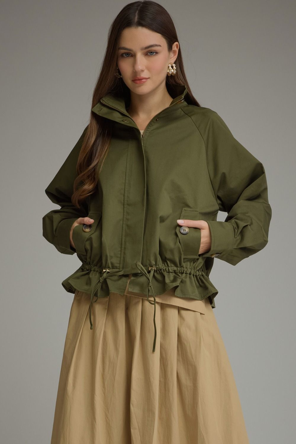 Woman wearing the Andrea olive green long sleeve jacket with a stand neck and drawstring hem.