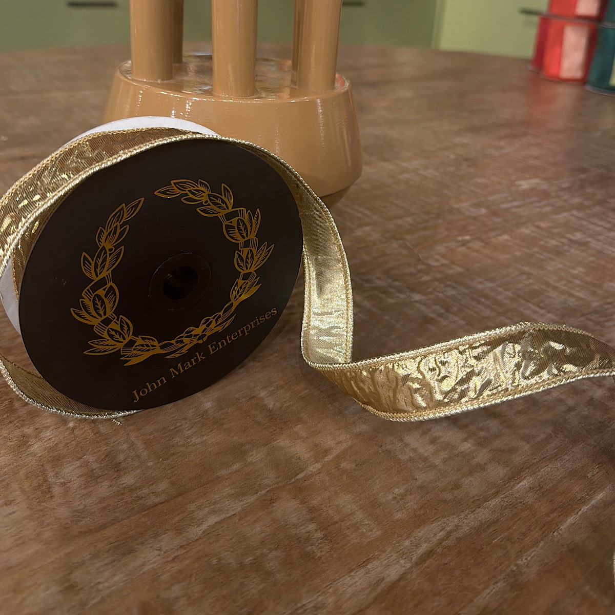Spool of 1x10yd crinkle metallic gold dupion fused ribbon on a wooden surface.