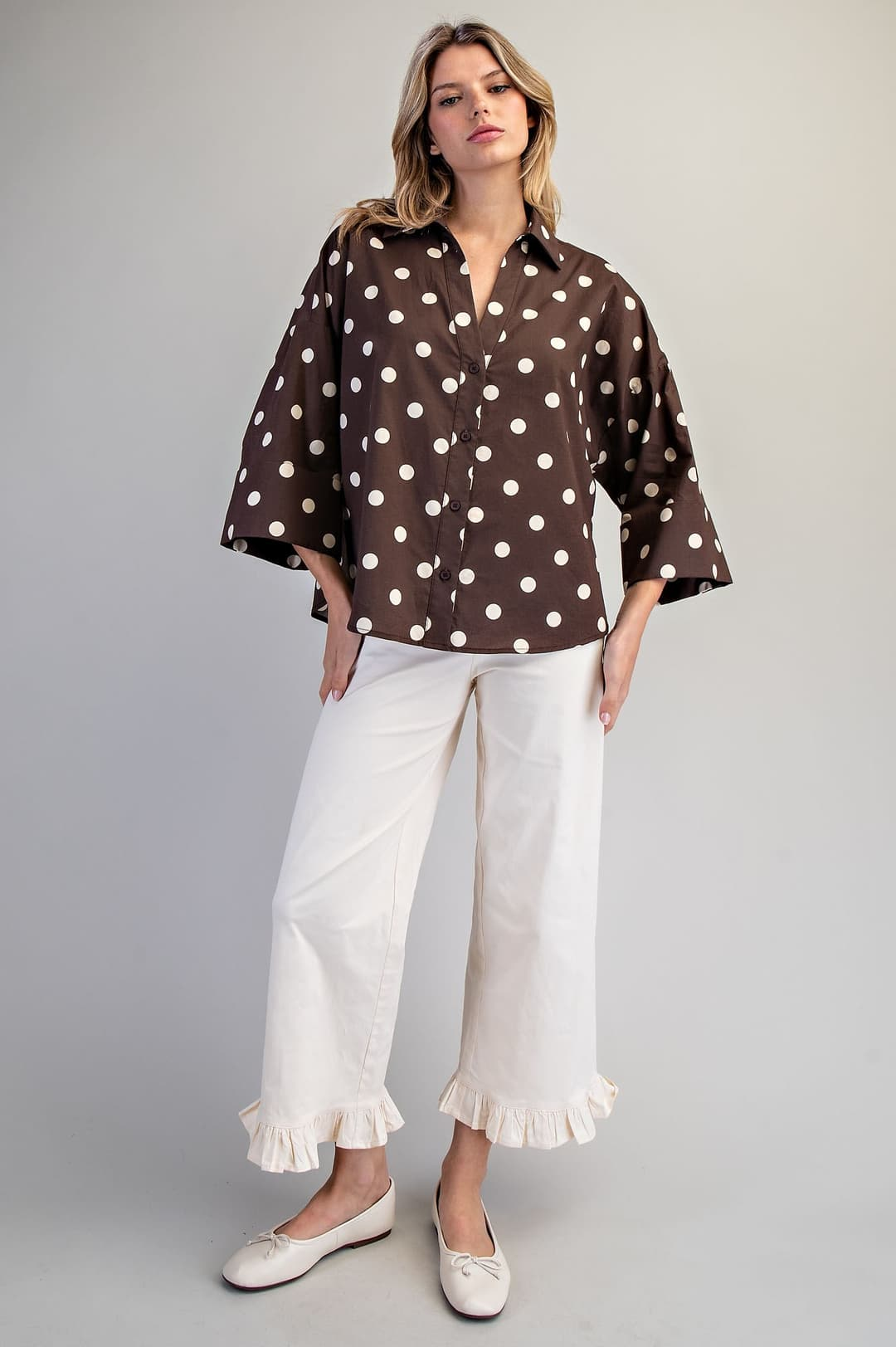 Woman wearing a brown oversized button-down blouse with white polka dots and wide dolman sleeves.