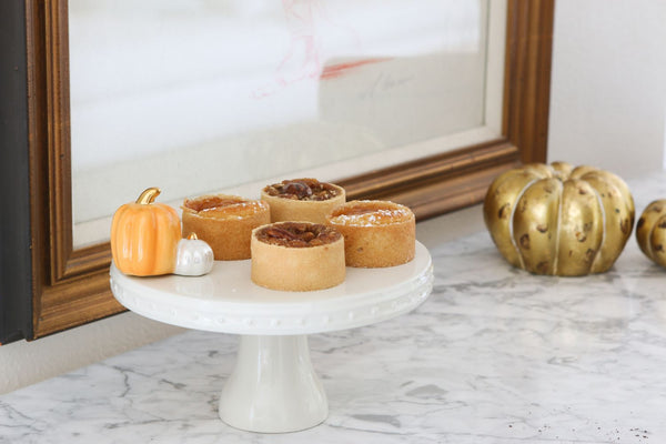 Four small pumpkin and pecan tarts on a white cake stand with decorative pumpkins.