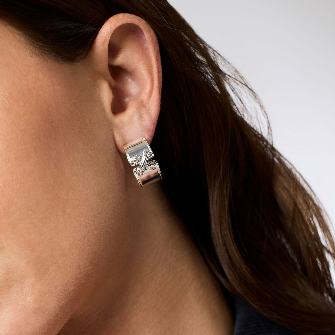 A person wearing a wide, polished silver Essex Hoop earring with a textured cross detail.
