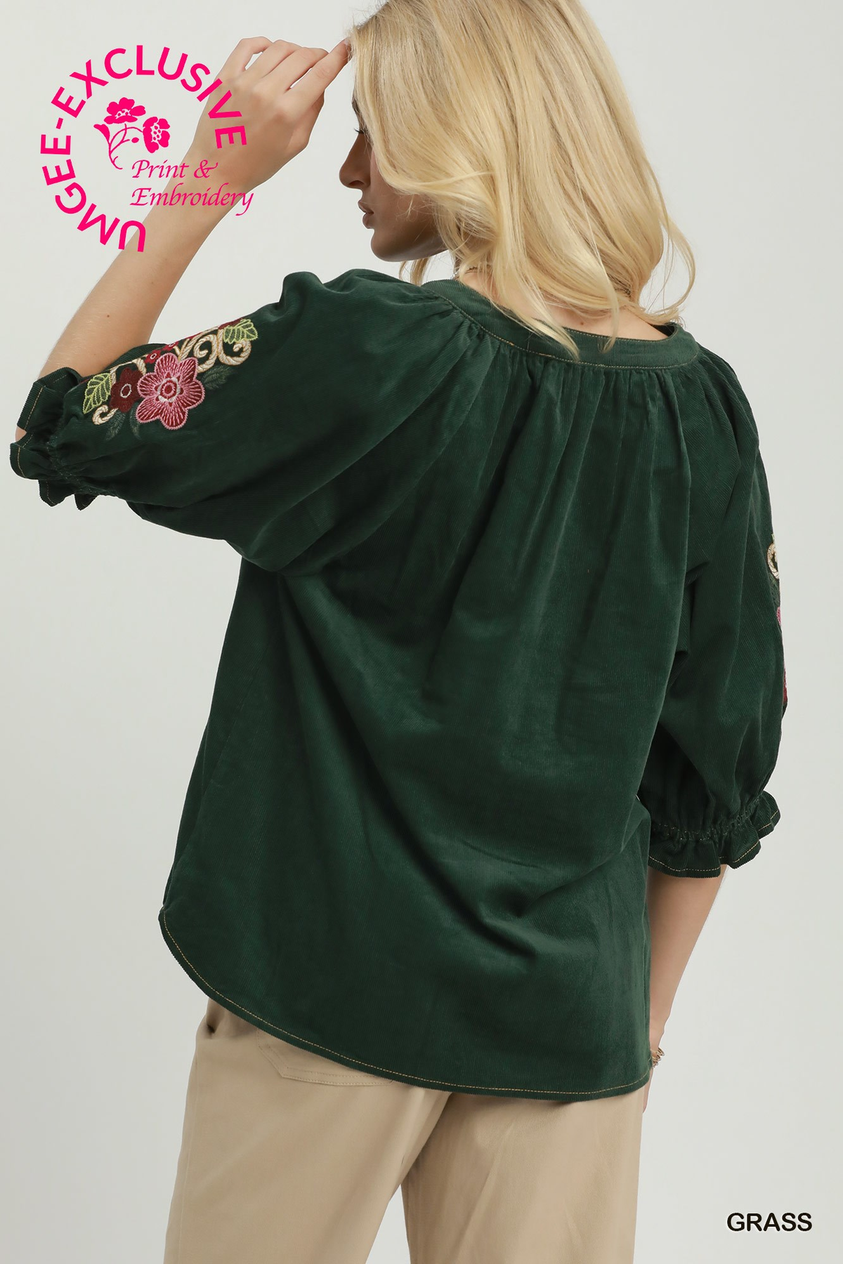 Back view of a woman wearing a dark green corduroy blouse with floral embroidery on the sleeves.