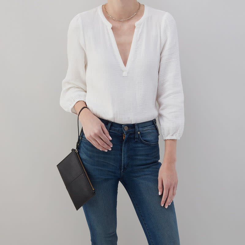 Black leather Vida small pouch with brushed antique brass hardware, D-ring strap, zip closure, and coconut shell interior.