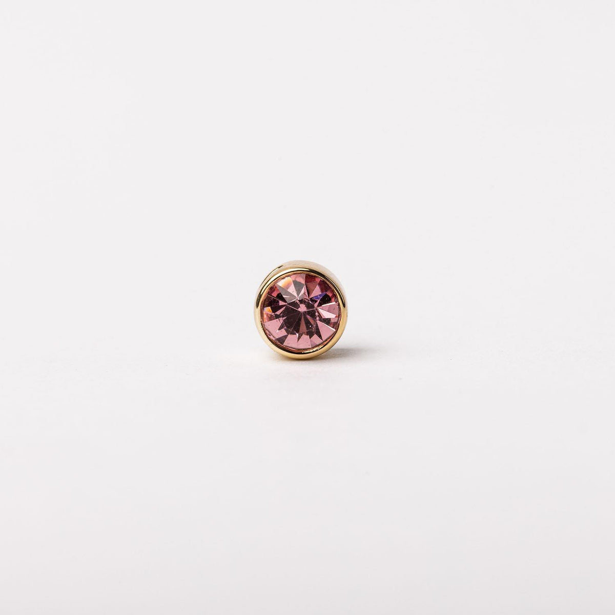 Round gold stud earring featuring a faceted pink gemstone in a bezel setting.