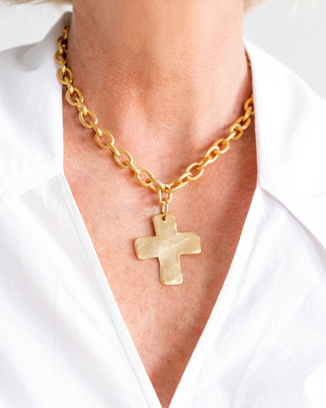 Close-up of a person wearing a gold-plated chunky chain necklace with a solid cross pendant.