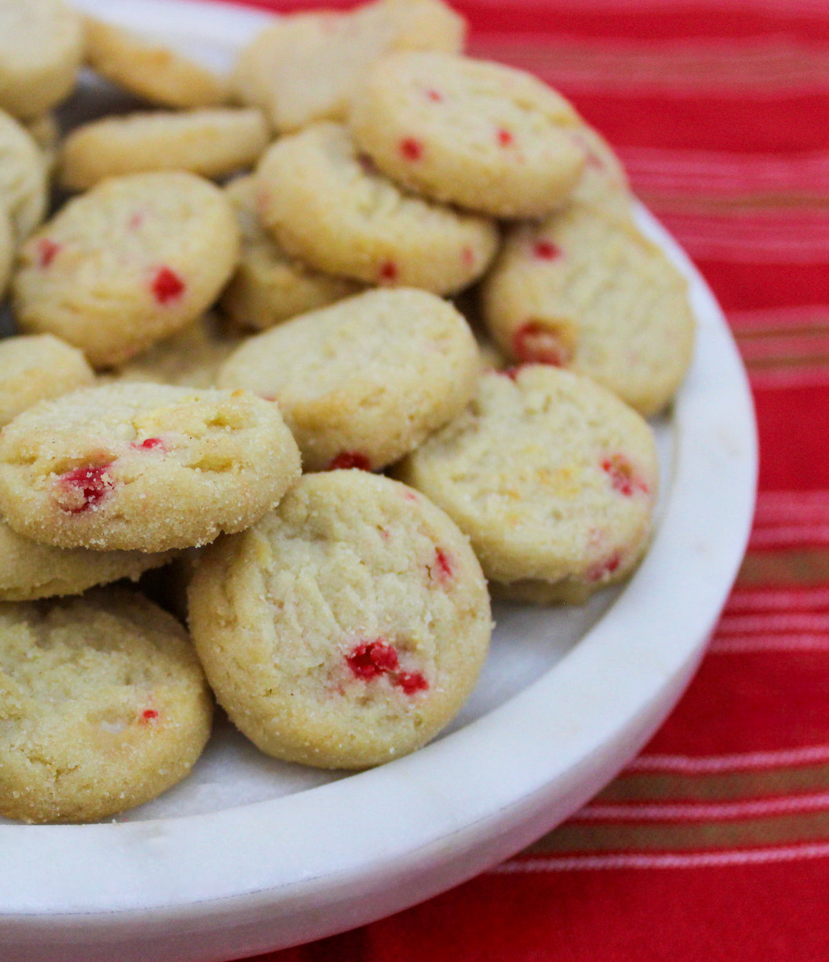 Round white chocolate peppermint shortbread cookies with red candy bits on a white plate.
