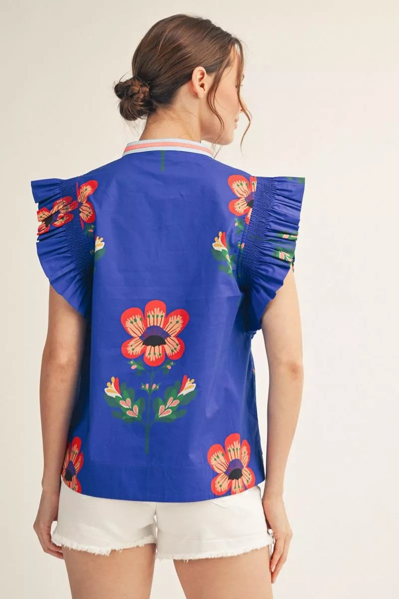 Woven top with ruffled sleeves, floral print, solid contrast notched v neckline, and smocking shoulder detail.