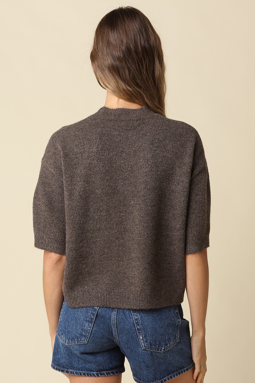 Back view of a woman wearing a brown Alice Parker half-sleeve sweater and blue denim shorts.