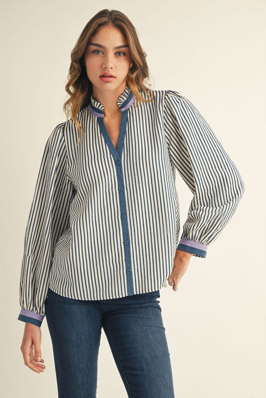 Woman wearing a blue striped long-sleeve button-down top with ruffled neckline and contrast binding.