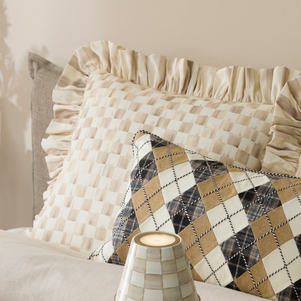 Mocha check throw pillow with a ruffled edge on a bed next to a diamond pattern pillow.