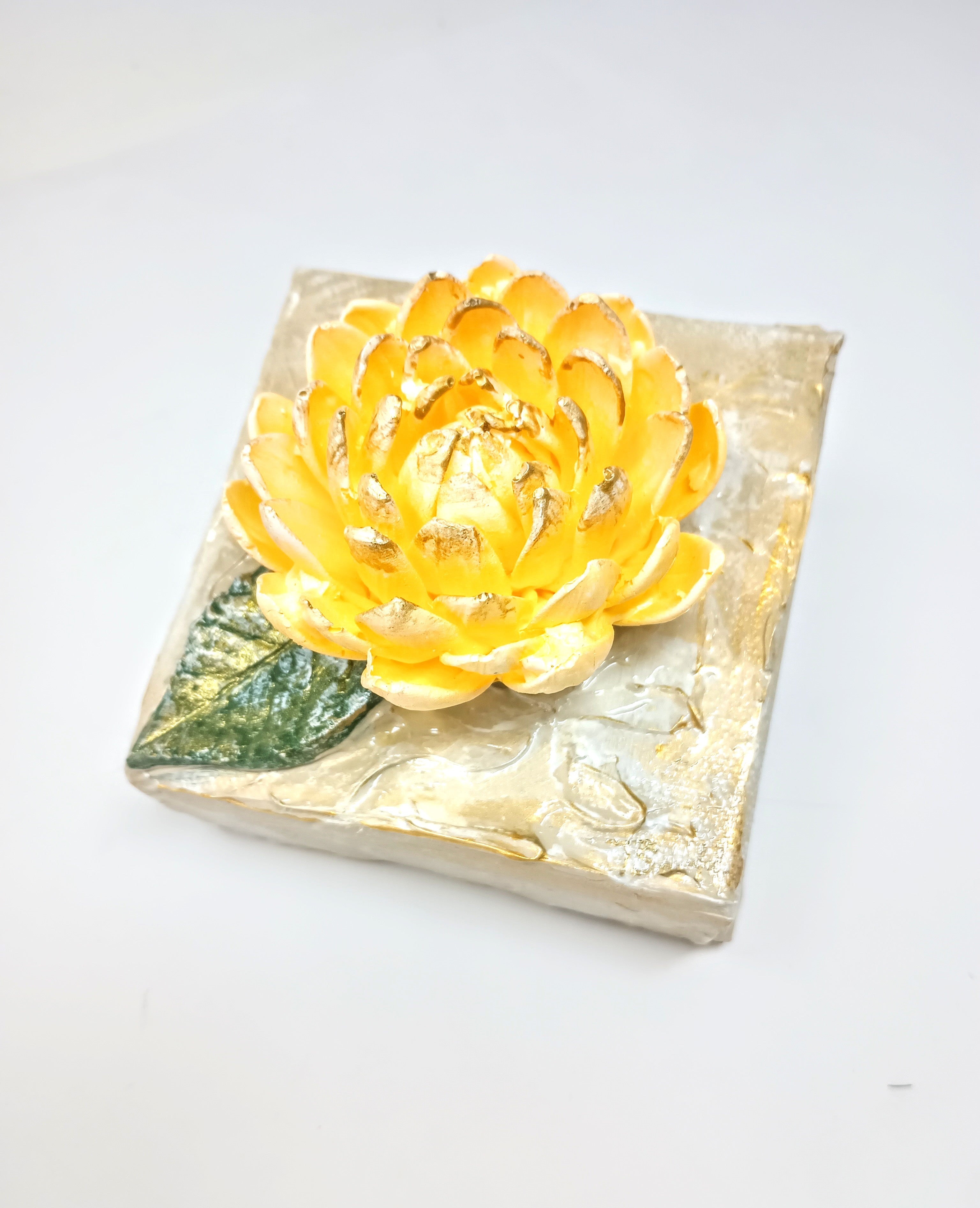 Square clay mum artwork featuring a sculpted floral relief in earthy tones on a textured surface.