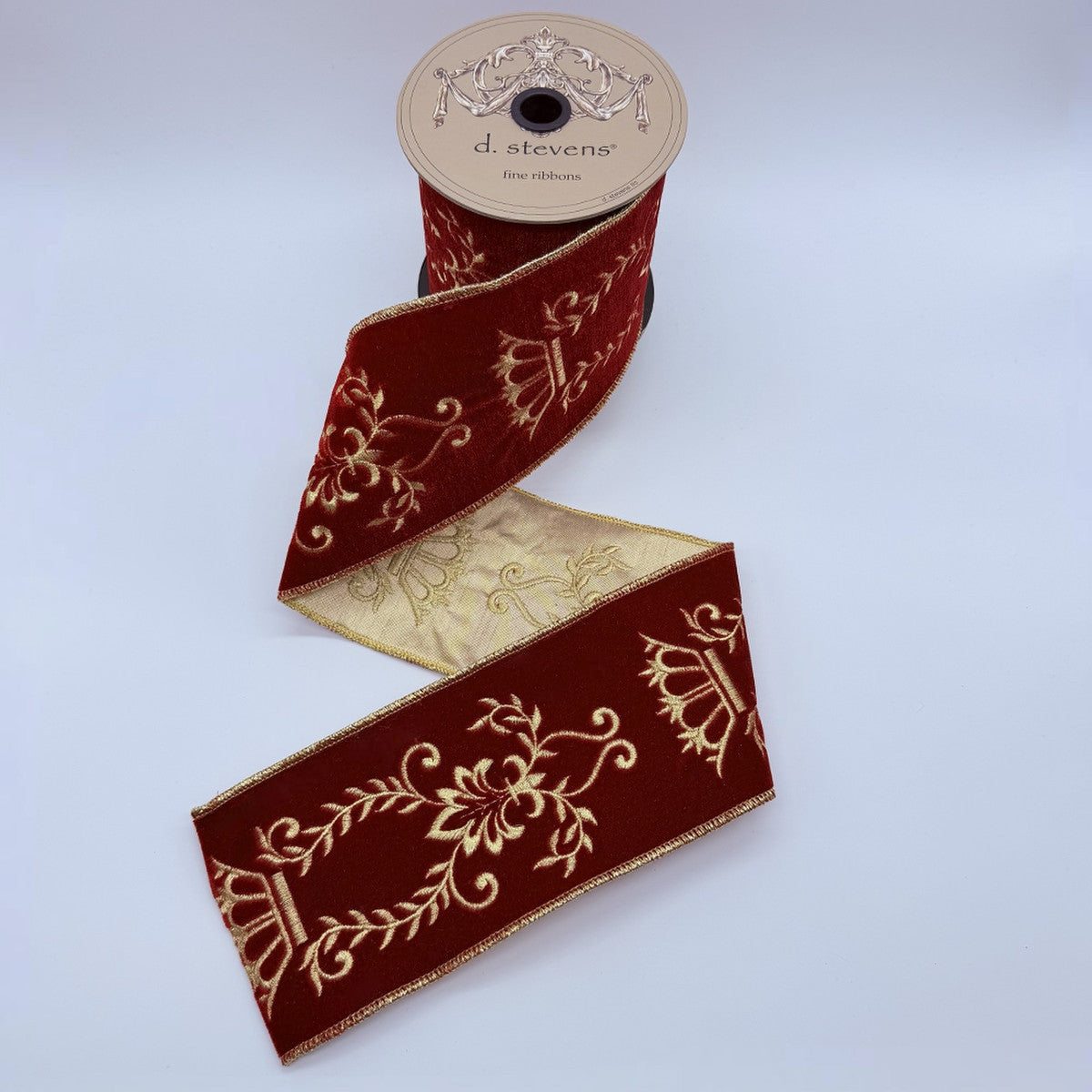 4 inch wide dark red velvet ribbon with gold majestic scroll embroidery on a spool.