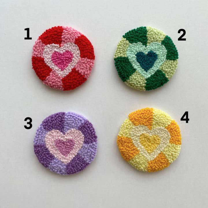 Four round punch needle car coasters with heart designs in red, green, purple, and yellow colors.