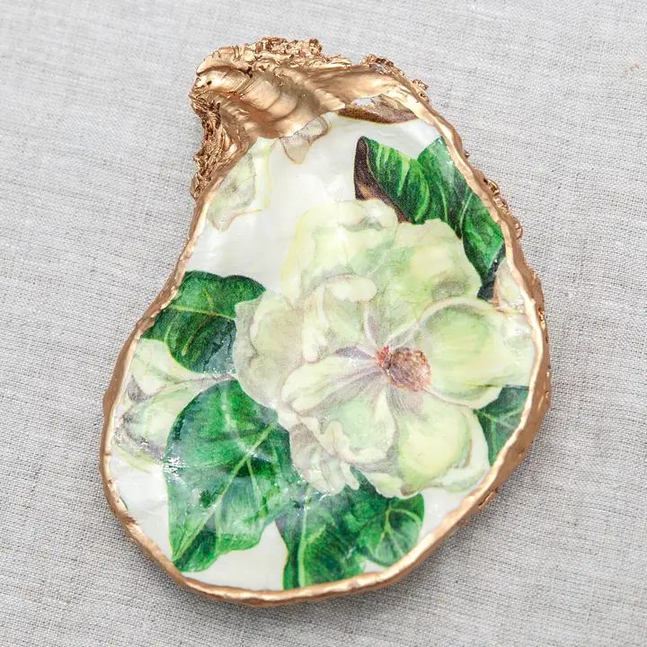 Decoupaged oyster shell with a white flower and green leaves design, trimmed in metallic gold.