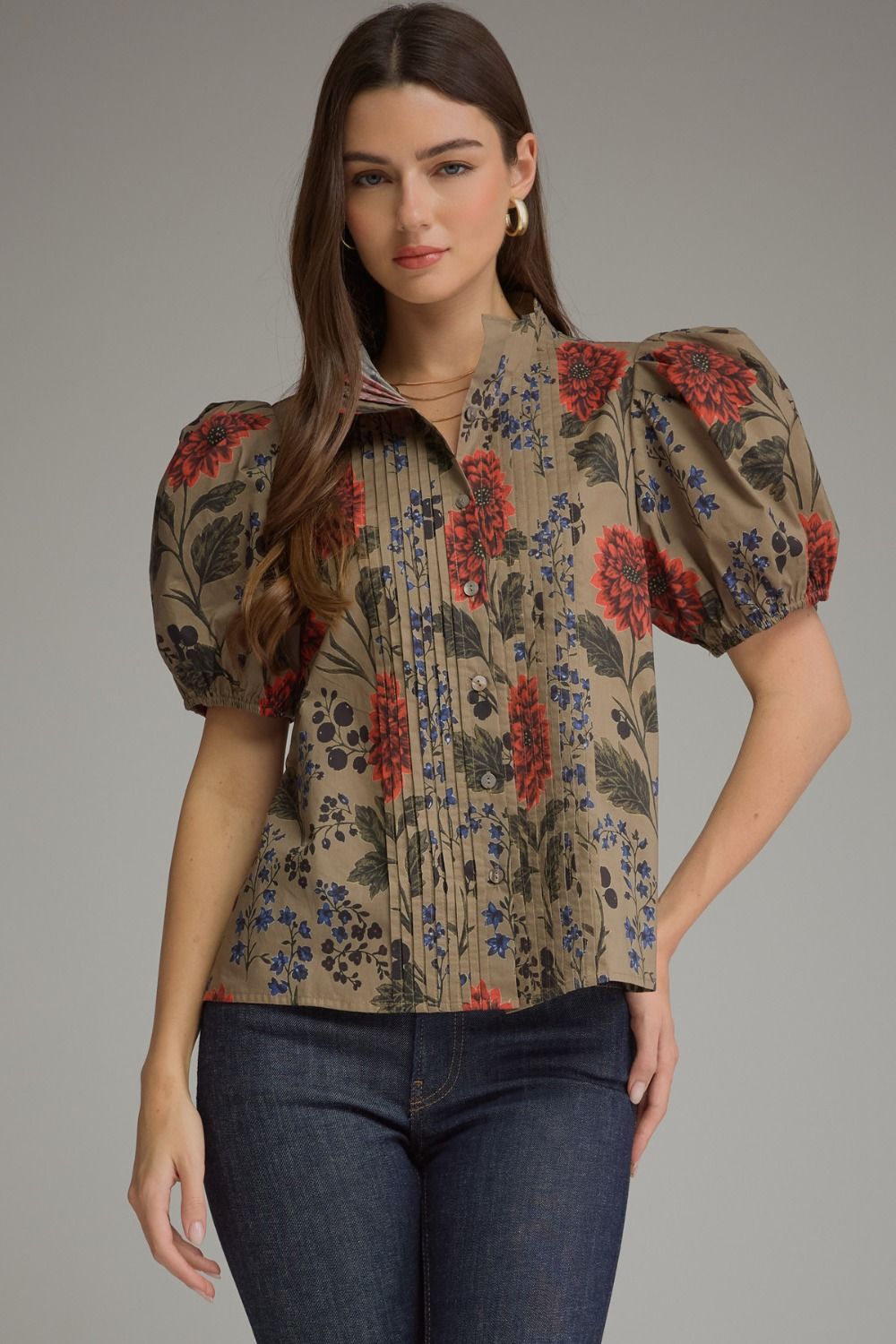Woman wearing a brown floral short puff sleeve top with pintuck details and dark blue jeans.