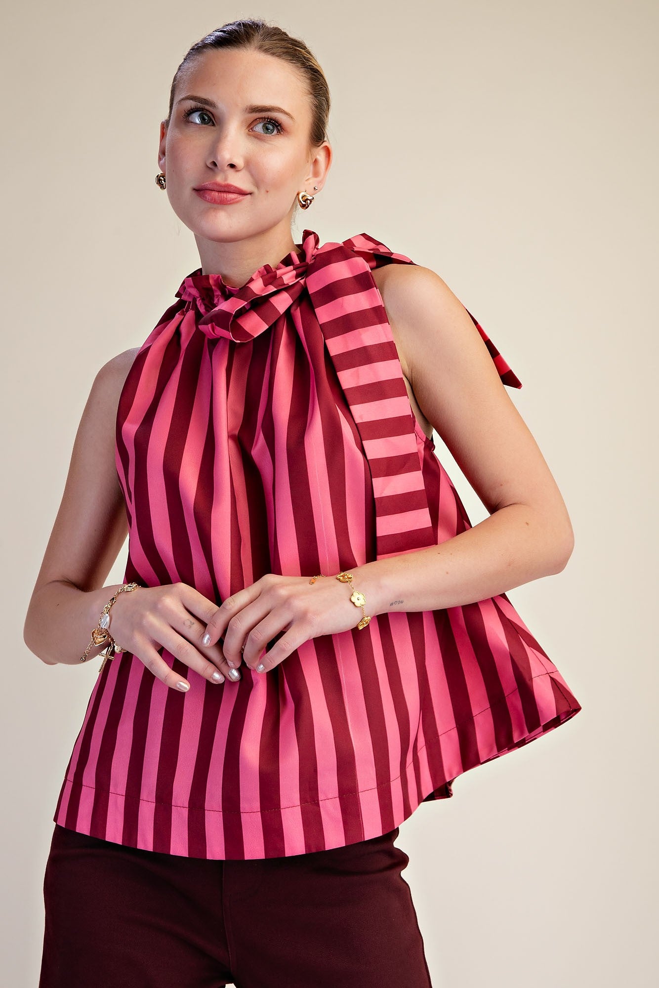Woman wearing a pink and burgundy vertical stripe sleeveless top with a ruffled tie neckline.