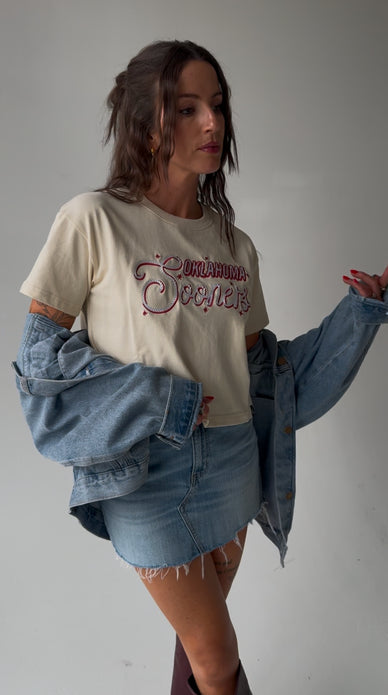 Woman wearing a cream Mandy Oklahoma Lasso Luxe Heavyweight Crop Tee with a denim skirt and jacket.