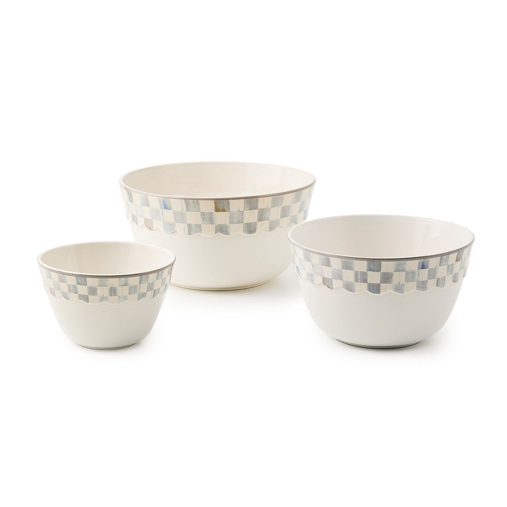 Three white stoneware mixing bowls in varying sizes with a blue and grey checkered rim pattern.