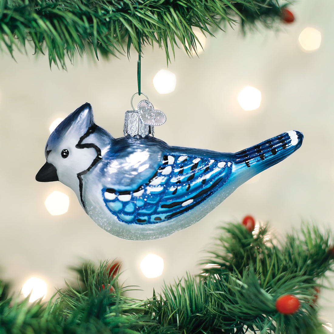 Bright blue jay glass ornament with glitter accents hanging on a Christmas tree branch.