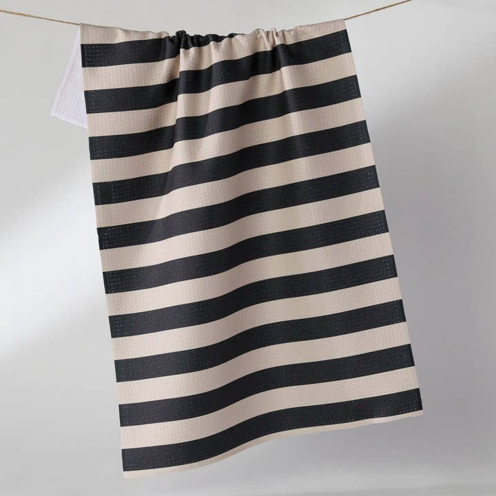 Black and beige horizontal striped waffle weave tea towel hanging on a clothesline.