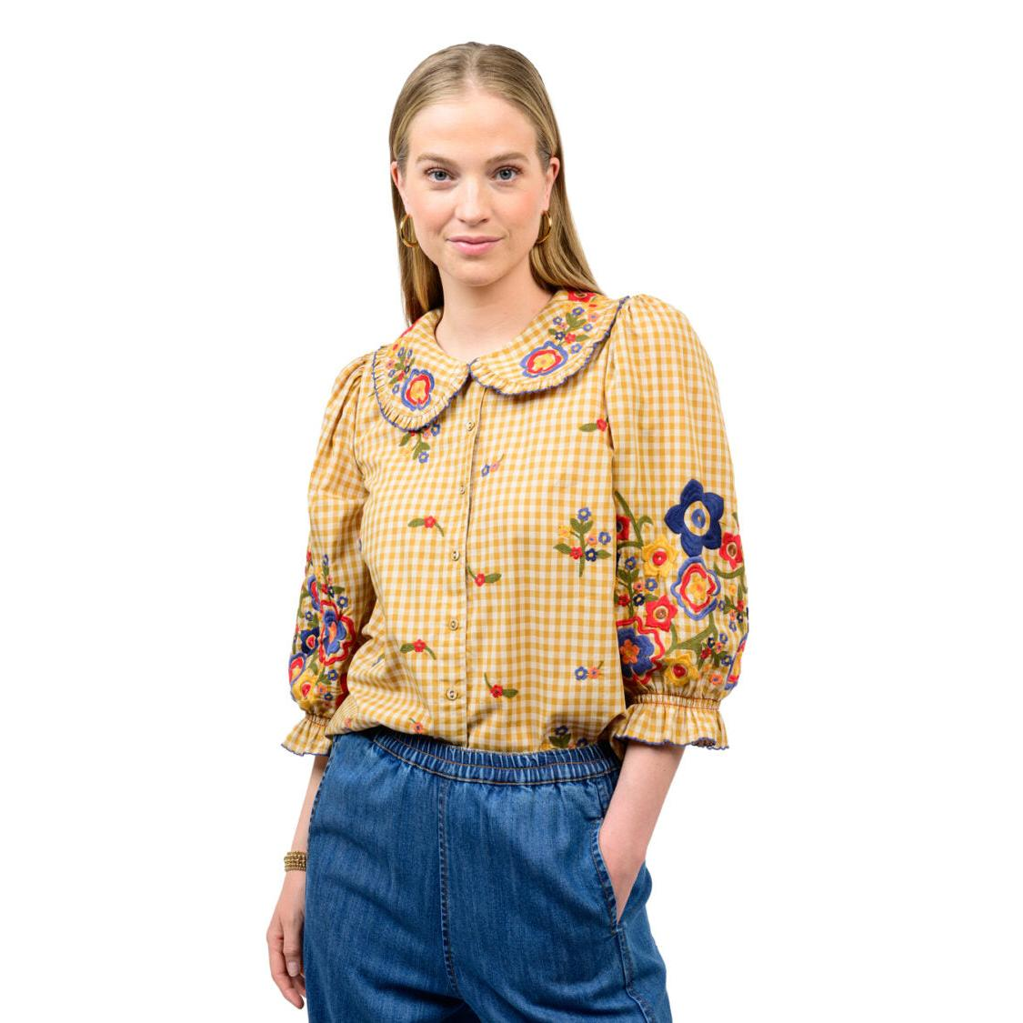 Woman wearing the Marian Check Garden Top in golden gingham with floral embroidery and denim pants.