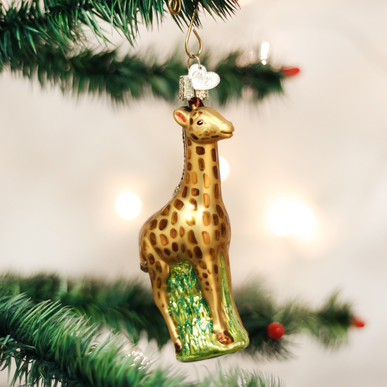 Glass baby giraffe Christmas ornament with gold spots hanging on a green tree branch.