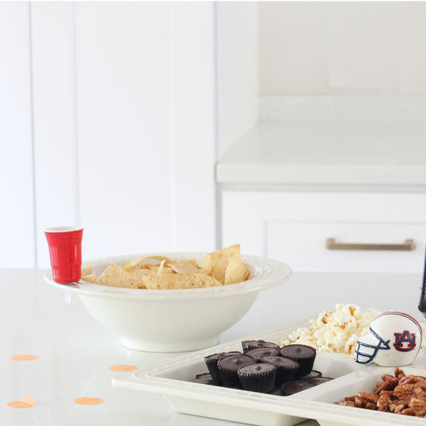 White ceramic serving bowl filled with tortilla chips and a red mini cup attached to the rim.
