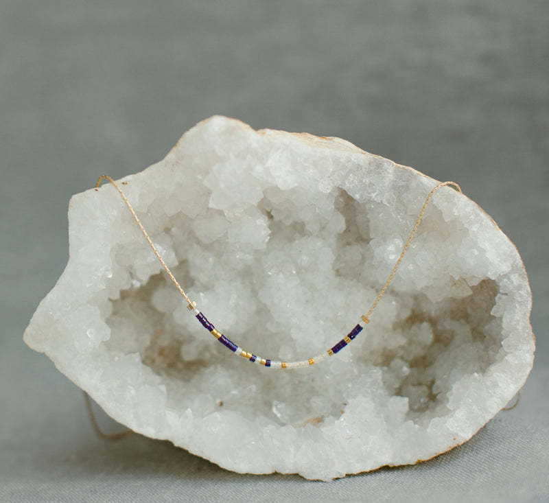Joshua 1:9 Morse code necklace with navy and cream beads on a gold chain, displayed on a geode.