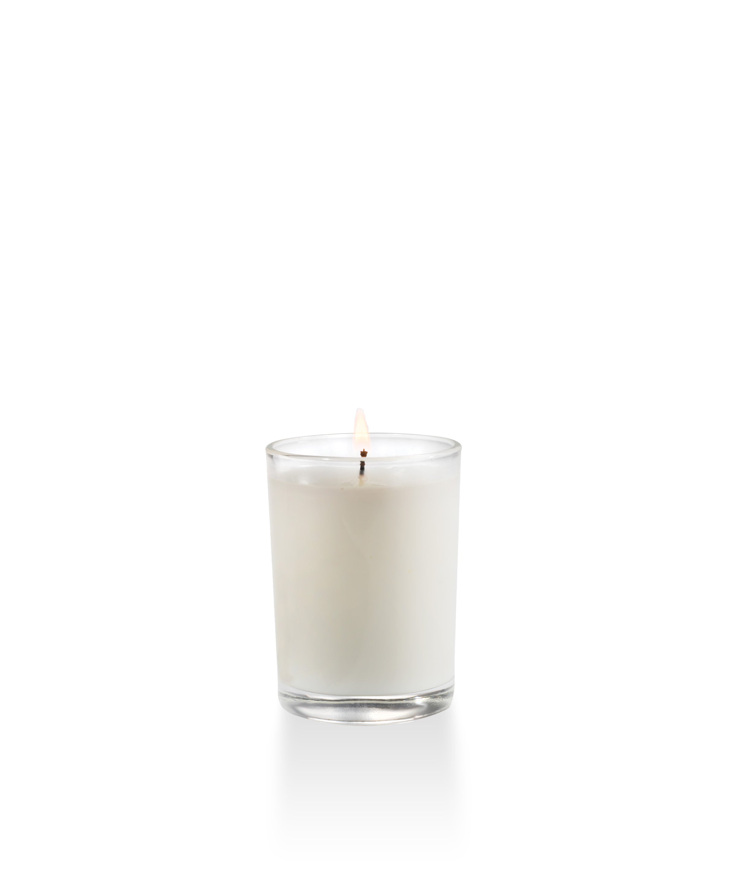 The Smell of Spring white votive candle in a clear glass cylinder with a lit wick.