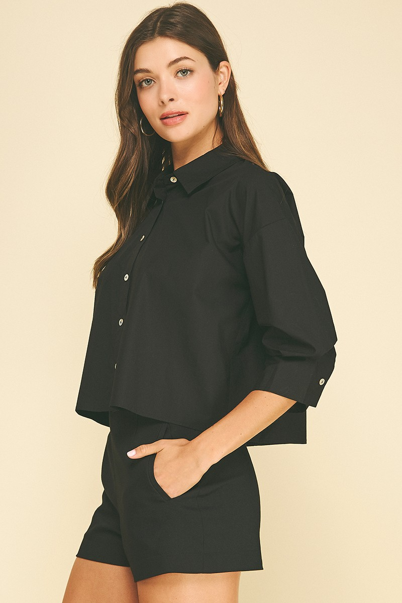 Woman wearing a black cropped button-down shirt with 3/4 tuck detailed sleeves and matching shorts.