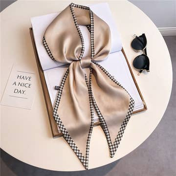 Beige double-layer head scarf with a houndstooth pattern border, tied in a bow on a white table.