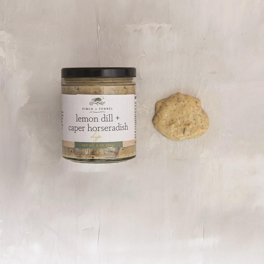 A jar of Finch + Fennel Lemon Dill + Caper Horseradish Dip next to a dollop of the creamy dip.