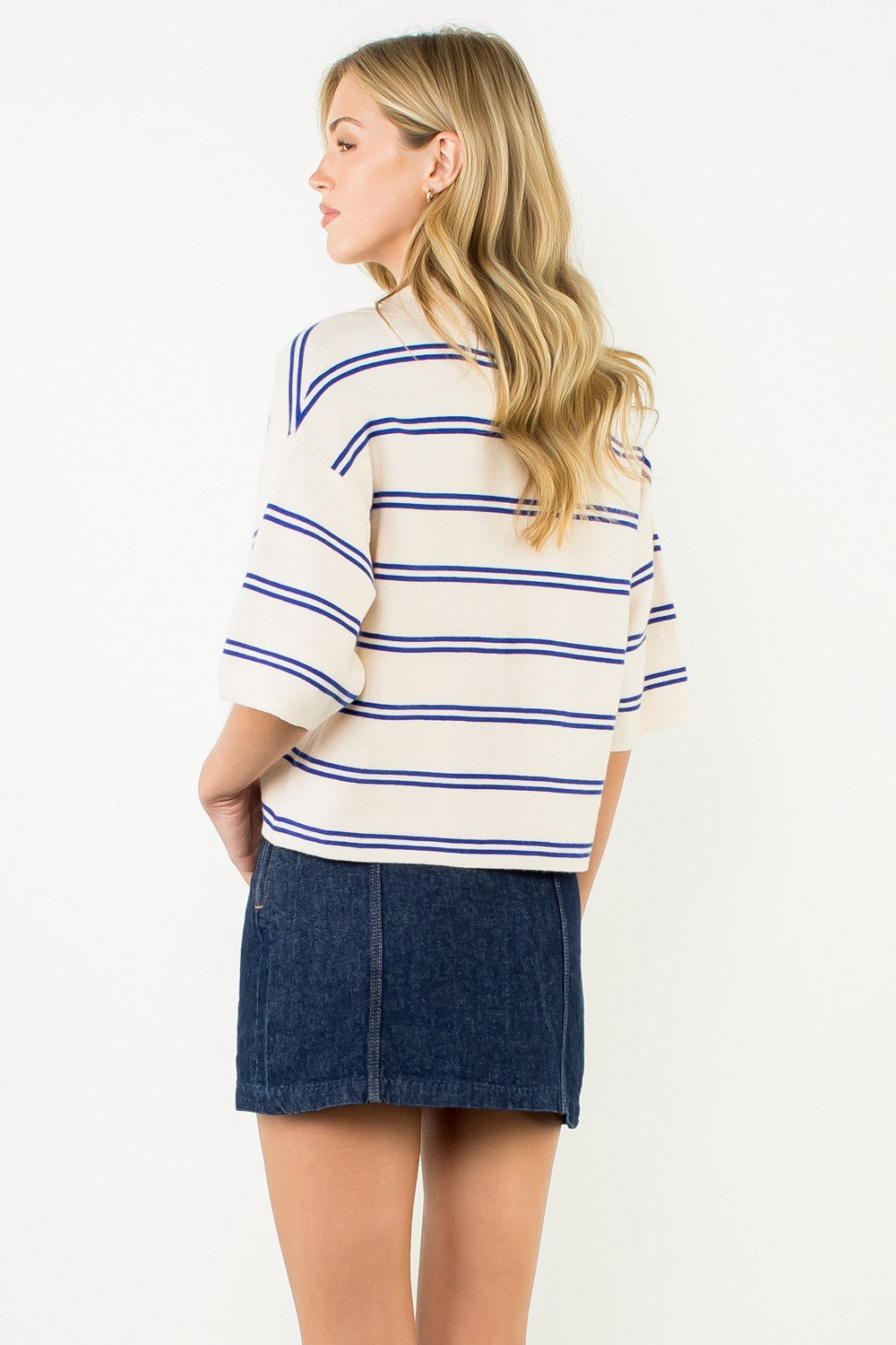 Back view of a woman wearing a cream and blue striped short sleeve knit top with a denim skirt.