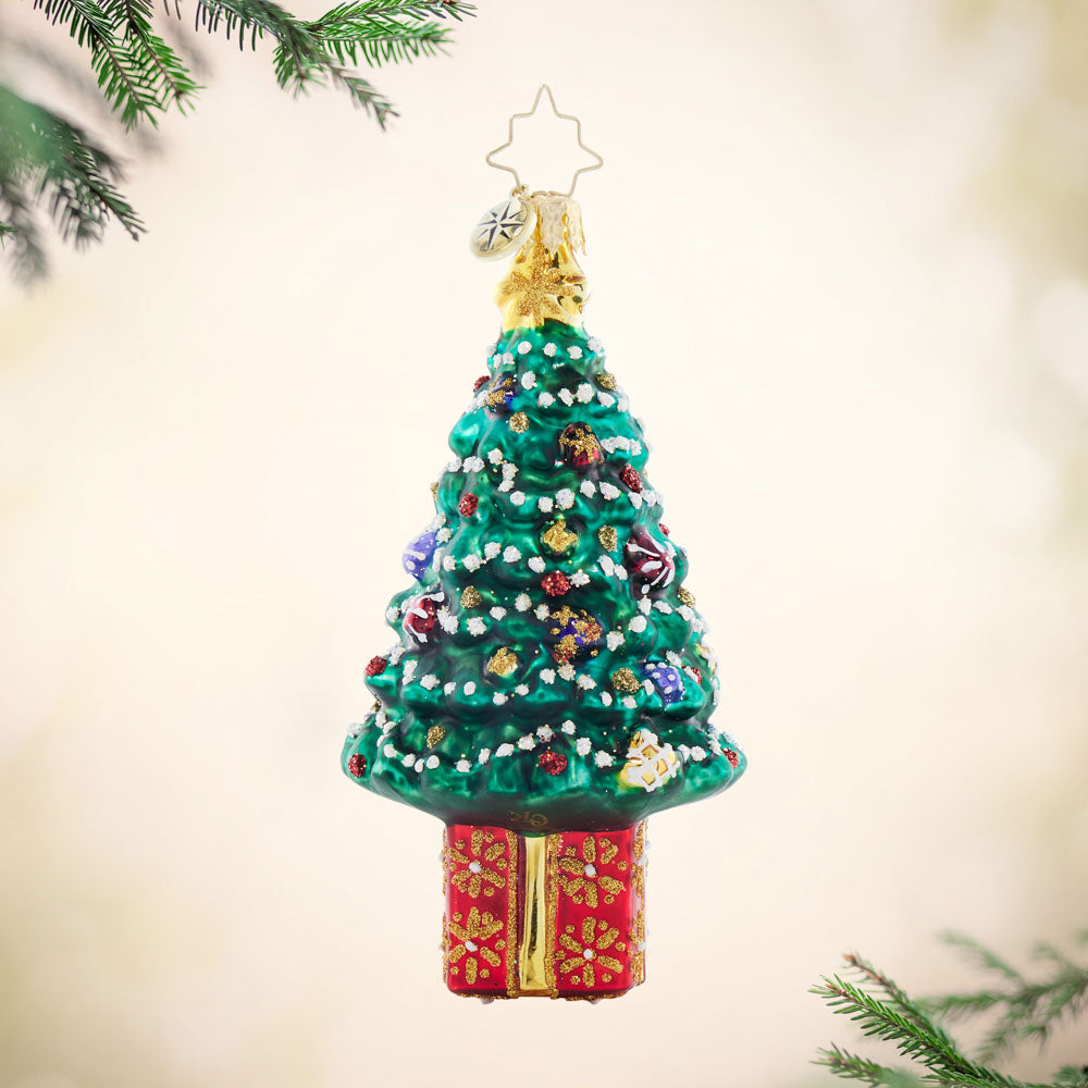 Glass Christmas tree ornament with a red gift box base, decorated with white snow and colorful baubles.