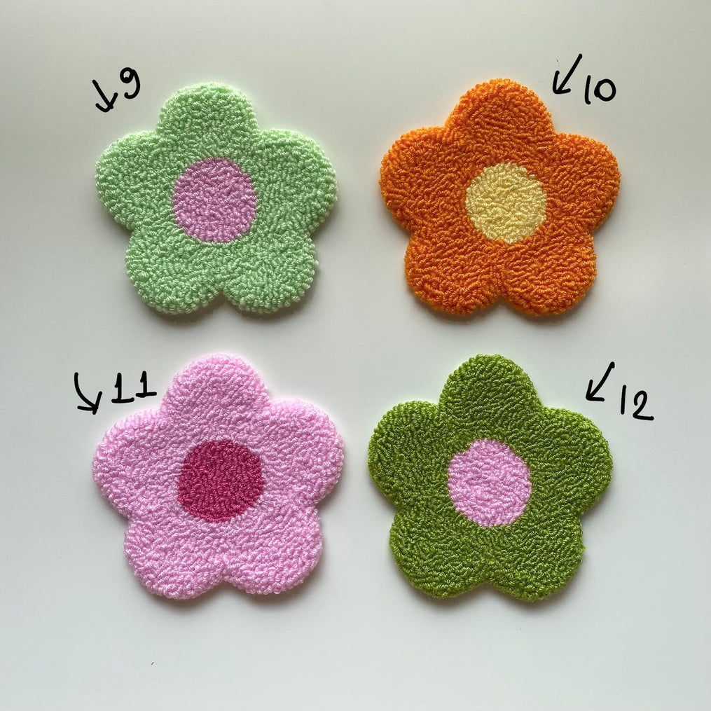 Four handmade flower-shaped punch needle coasters in green, orange, pink, and olive green.