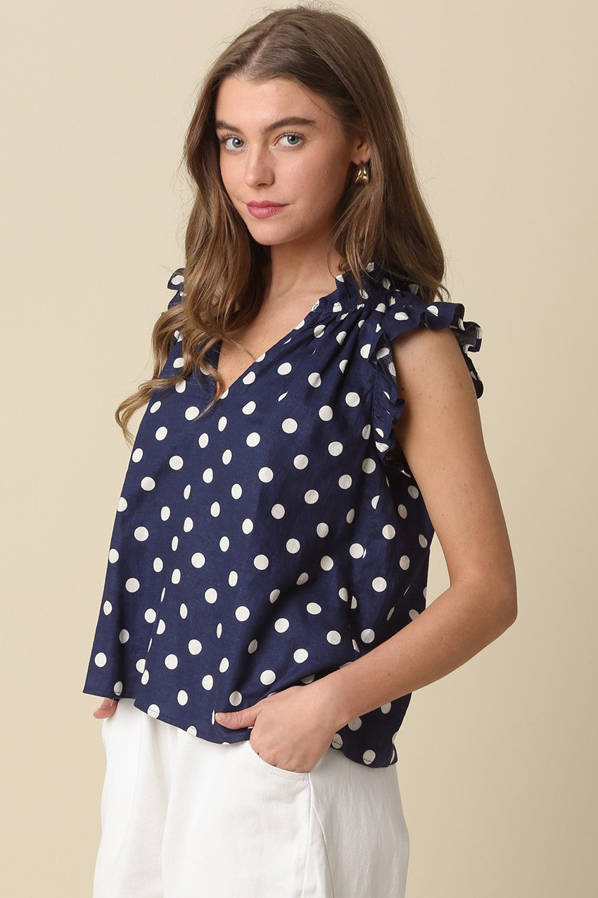 Woman wearing a navy blue Mira Polka Dot Ruffle Blouse with white dots and white pants.