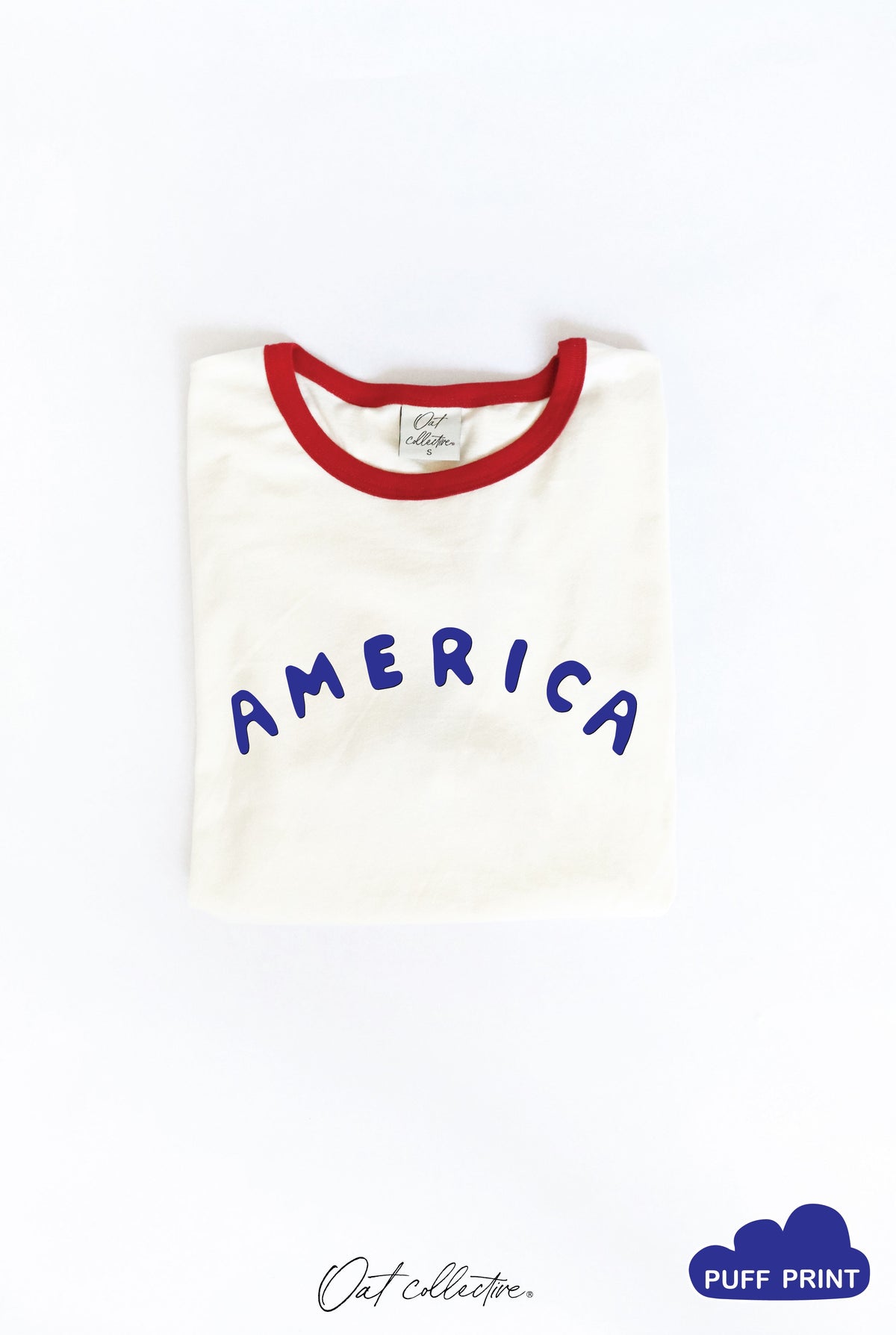 White ringer tee with a red neckline and blue puff print "AMERICA" graphic across the chest.