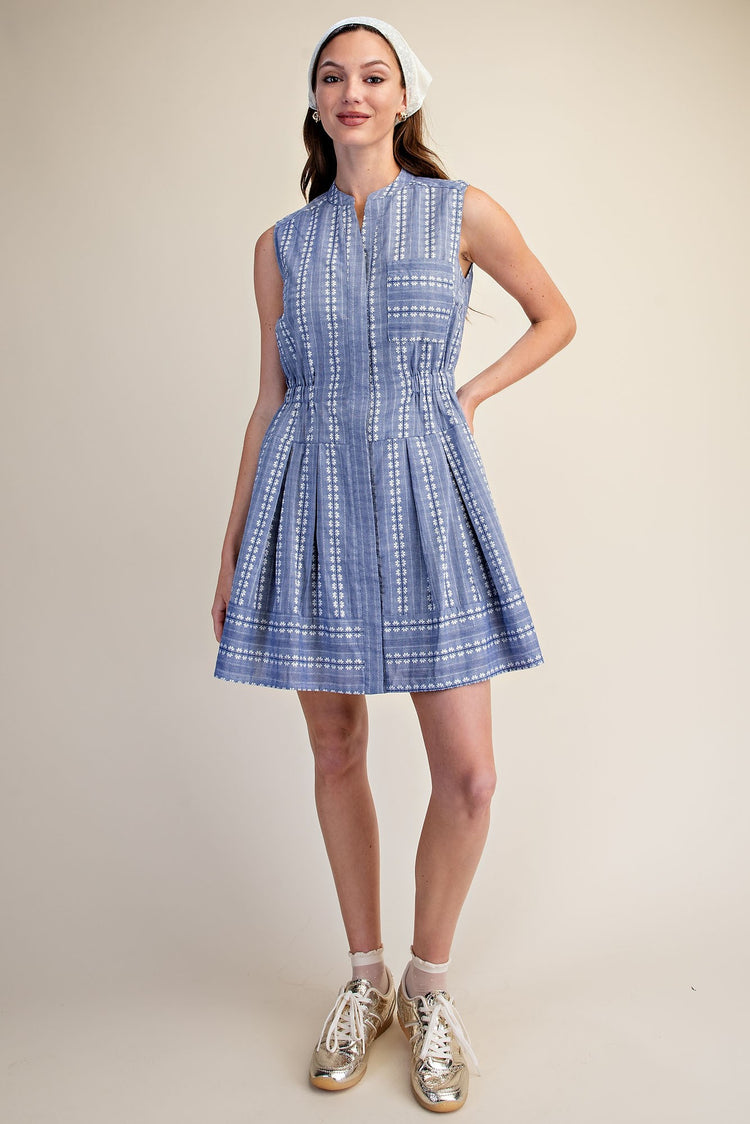 Woman in a blue sleeveless Clara Boho shirt dress with white embroidery and a pleated skirt.