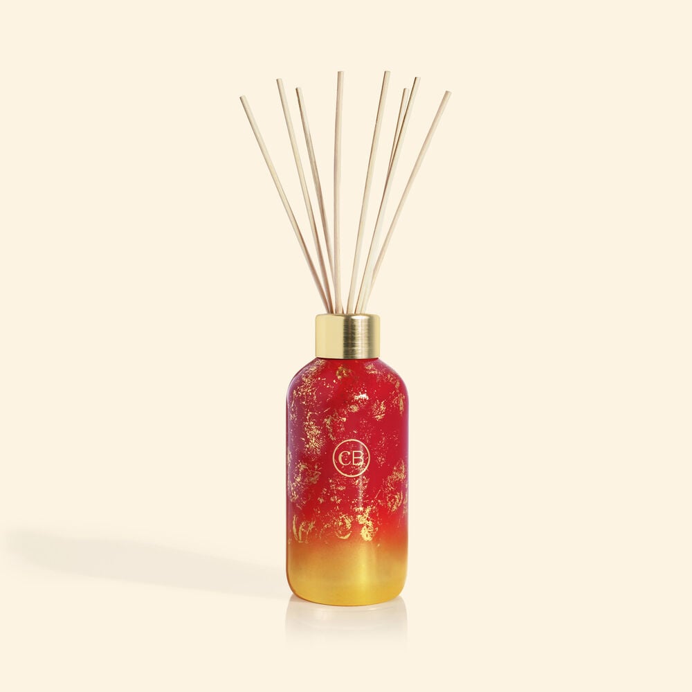 Apple Cider Social Glimmer Reed Diffuser in a clear glass vase with floating decorative stones and reed sticks.