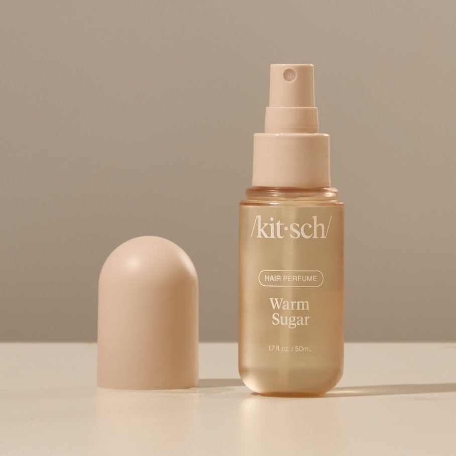 Small bottle of Warm Sugar hair perfume with a white cap against a neutral background.