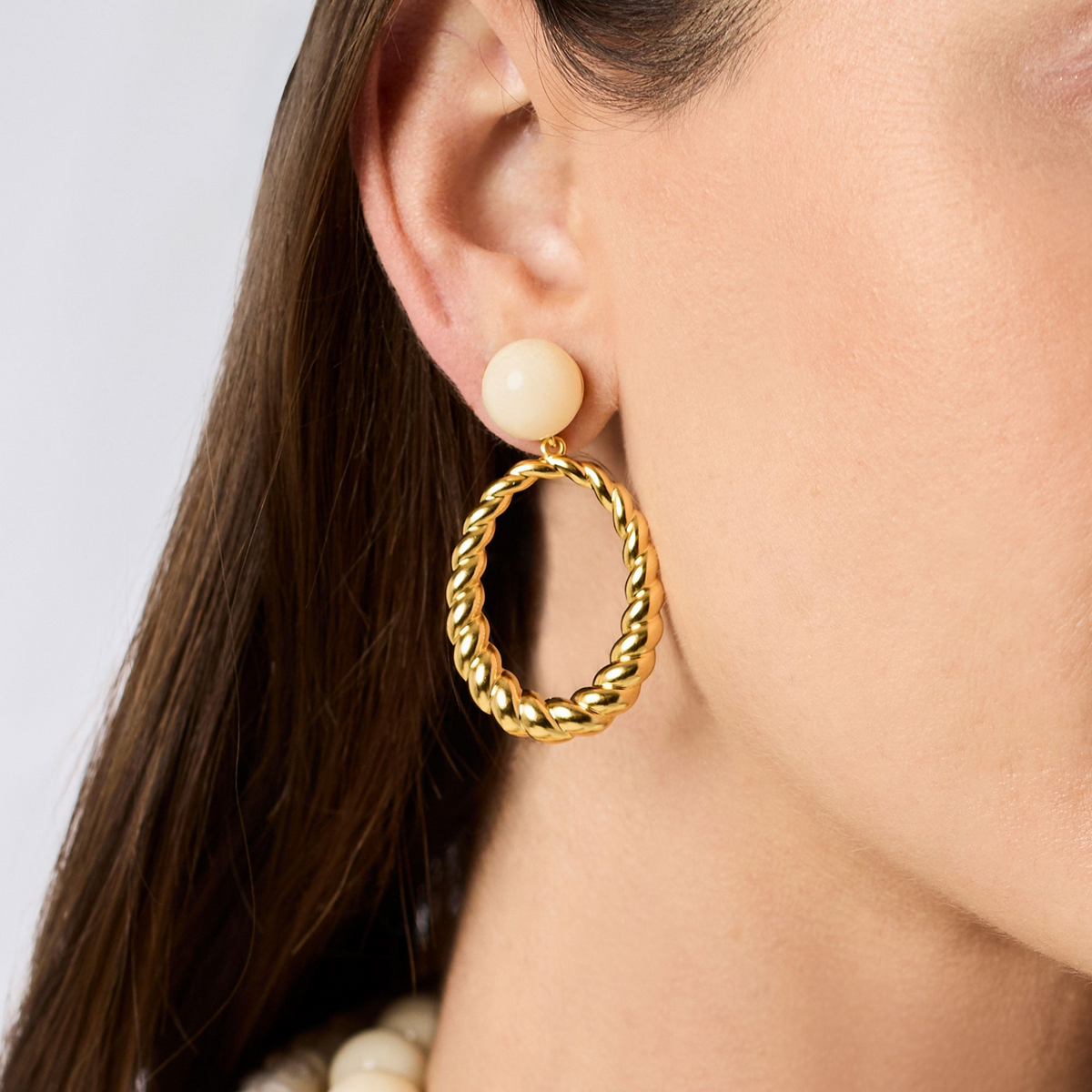 A woman wearing a Ravello Statement Earring featuring a cream resin stud and a gold twisted hoop.