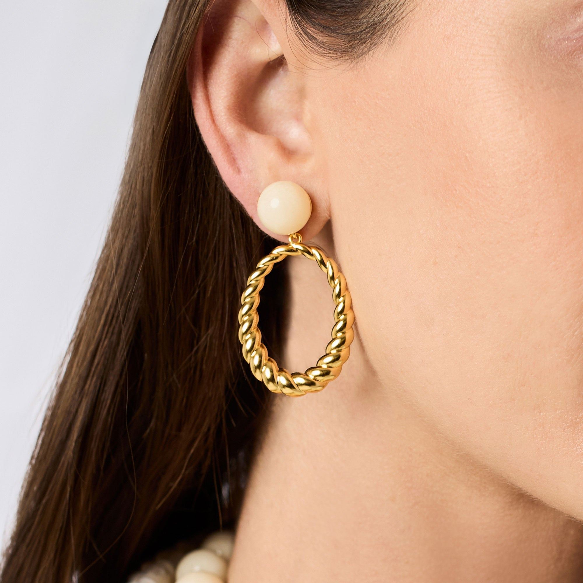 A woman wearing a Ravello Statement Earring featuring a cream resin stud and a gold twisted hoop.