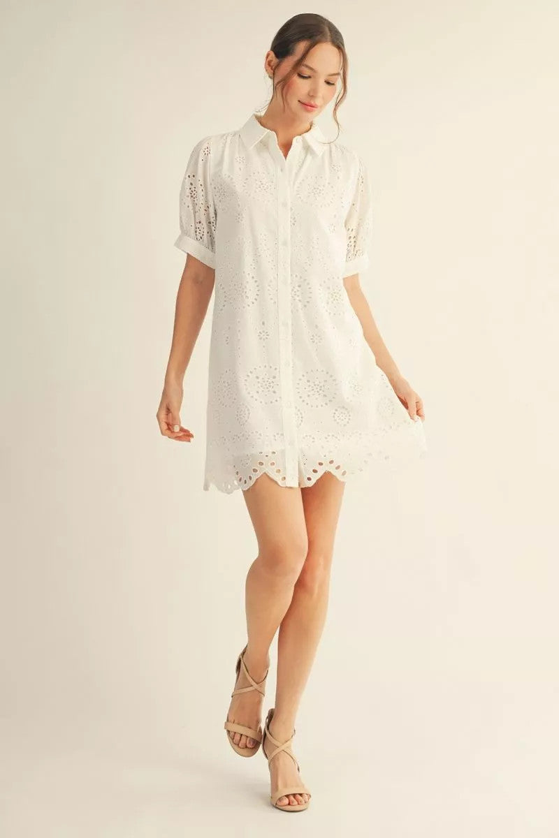 Woman wearing a white Eleanor short sleeve button down eyelet dress with a scallop hem.