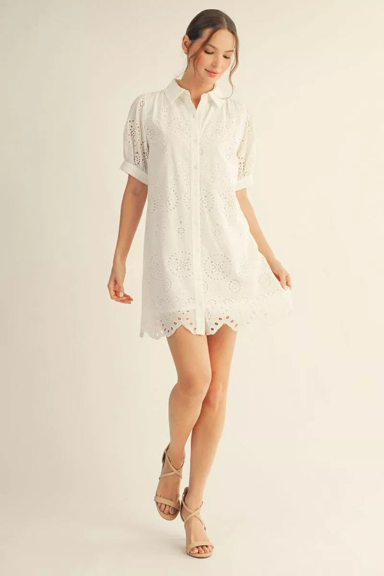 Woman wearing a white Eleanor short sleeve button down eyelet dress with a scallop hem.